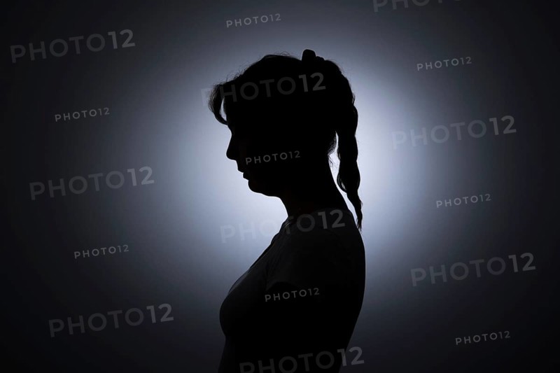 Symbolic photo on the subject of loneliness in woman. The silhouette of a young woman stands out against a white wall. Berlin, 22.08.2024