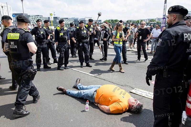 An activist of the Last Generation weighing about 140kg with shirt Parents are liable for their children! lies on the street and is observed by surrounding police officers during the occupation of Rahel-Deer-Straße in front of Berlin Central Station, Berlin, 25 May 2024