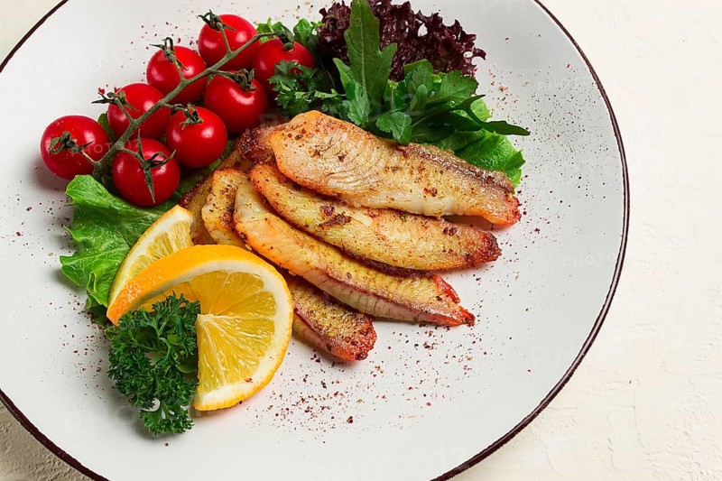 Fried Tilapia fish fillet, in spices, with cherry and salad, on a white plate, homemade, no people