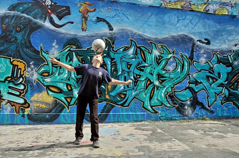 A ten-year-old boy plays with his football in front of a graffiti wall, Germany, Europe