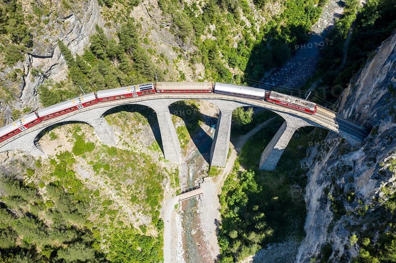 Drone shot of train passing the Landwasserviadukt near Filisur, red train of Bernina Express, Switzerland, Europe