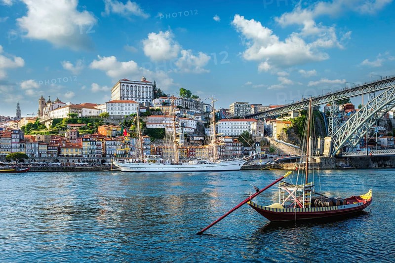 View of Porto city and Douro river with traditional boats with port wine barrels and sailing ship from famous tourist viewpoint Marginal de Gaia riverfront. Porto, Vila Nova de Gaia, Portugal, Europe