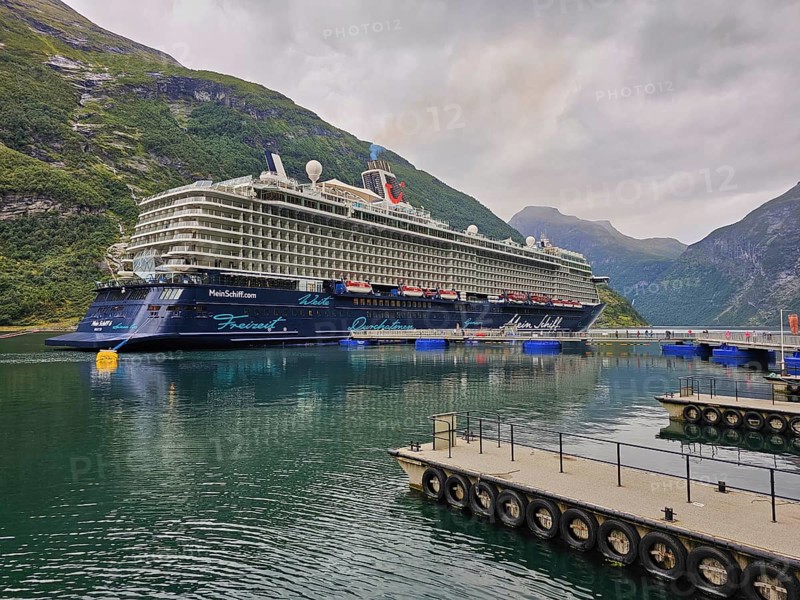 A large cruise ship, Mein Schiff 6, lies in the fjord, surrounded by green mountains under a cloudy sky, with catwalk, Geiranger, Geiranger Fjord, Stranda, Romsdal, Norway, Europe