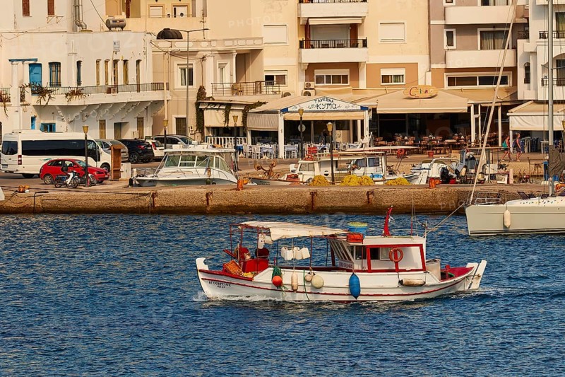 A small boat sails along the shore in a harbour with various buildings and boats, fishing boat, Pigadia, town and harbour, Pigadia Bay, main town, Karpathos, Dodecanese, Greek Islands, Greece, Europe