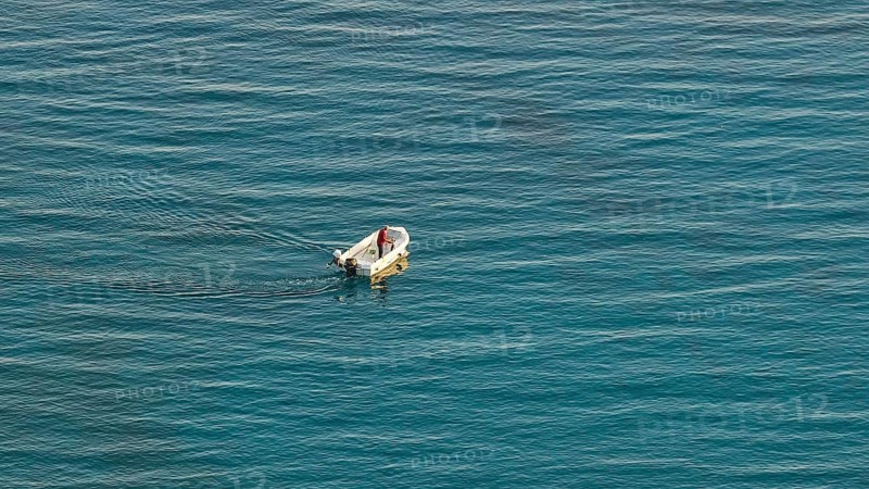 Single boat with one person on calm blue sea in the distance, Anthony Quinn Bay, Vagies Bay, Rhodes, Dodecanese, Greek Islands, Greece, Europe