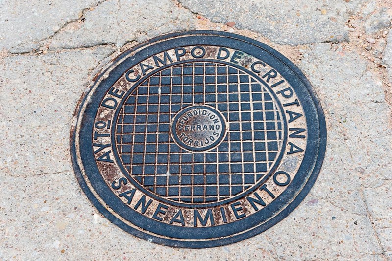A round metal manhole cover with text engraving on a tarmac road, manhole cover, Campo de Criptana, Ciudad Real province, Castilla-La Mancha, Don Quixote route, Spain, Europe