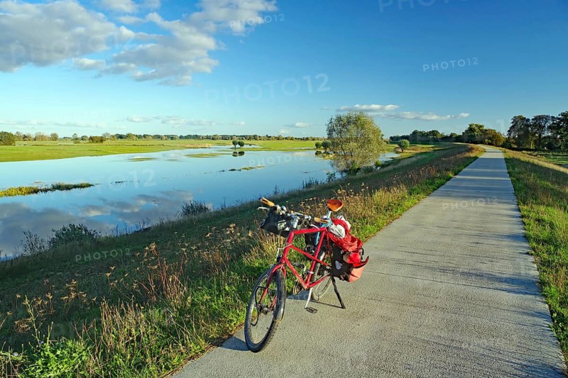 A bicycle stands on a concrete path next to a calm river under a clear blue sky with scattered clouds, bicycle tourism, autumn, Elbe, Langendorf, Wendland, Lower Saxony, Germany, Europe