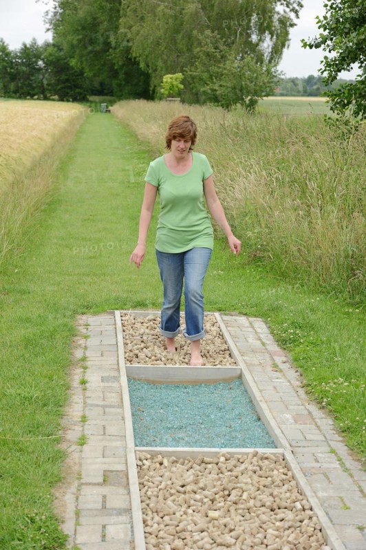 Woman walking barefoot over glass gravel and bottle corks, barefoot path Tilbeck Abbey, Havixbeck, North Rhine-Westphalia, Germany, Europe