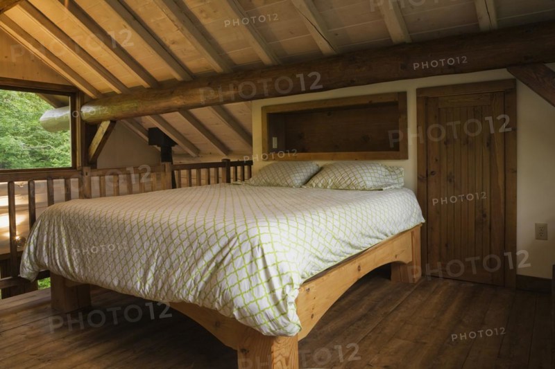 King size bed with pine wood frame in sparsely furnished Zen stmaster bedroom on mezzanine inside Scandinavian hybrid style log cabin home, Quebec, Canada, North America
