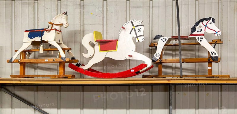 Three wooden rocking horses in a line on display in auction room, UK