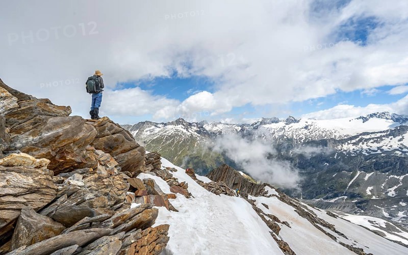 Mountaineer on a rocky ridge with snow, descent from the summit of Schönbichler Horn, view of snow-covered mountain peaks and valley Zemmgrund, Berliner Höhenweg, Zillertal Alps, Tyrol, Austria, Europe