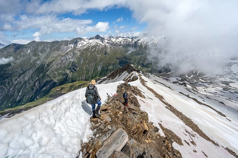 Mountaineer on a rocky ridge with snow, descent from the summit of Schönbichler Horn, view of snow-covered mountain peaks and valley Zemmgrund, Berliner Höhenweg, Zillertal Alps, Tyrol, Austria, Europe