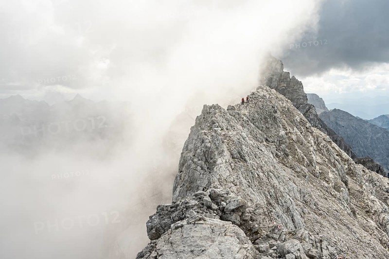 Clouds move around narrow rocky mountain ridge with mountaineers, Watzmann crossing to Watzmann Mittelspitze, view of mountain panorama, Berchtesgaden National Park, Berchtesgaden Alps, Bavaria, Germany, Europe
