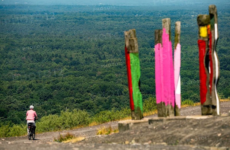 The Haniel spoil tip, 185 metre high spoil tip, at the Prosper Haniel mine, closed in 2019, artwork Totems by the sculptor Augustin Ibarrola, cyclist, in the background the Hiesfelder Wald forest and the Kirchheller Heide, Bottrop, Germany, Europe