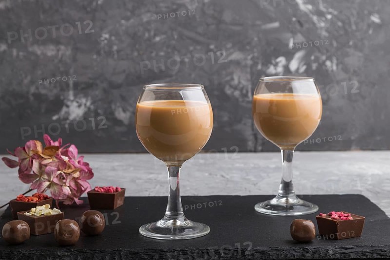Sweet chocolate liqueur in glass with chocolate candies on a gray concrete background and black stone slate board. Side view, close up