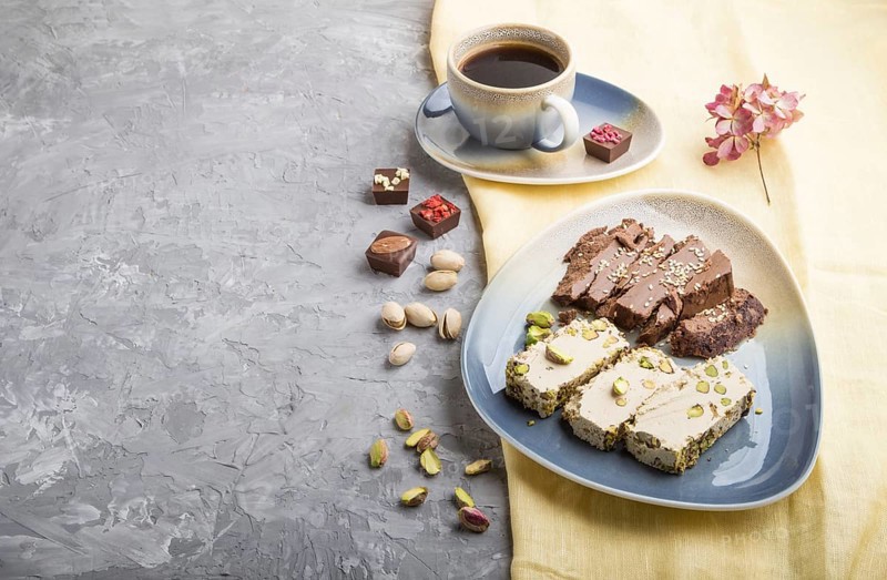 Traditional arabic sweets sesame halva with chocolate and pistachio and a cup of coffee on a gray concrete background and yellow textile. side view, copy space