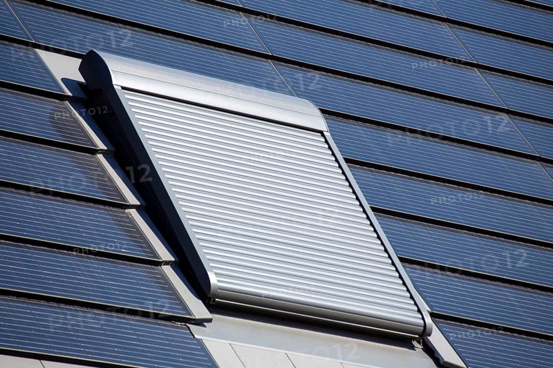 Roof window with roller shutter on a detached house with photovoltaic tiles. Photovoltaic tiles are a beautiful and high-quality alternative to conventional solar roofs