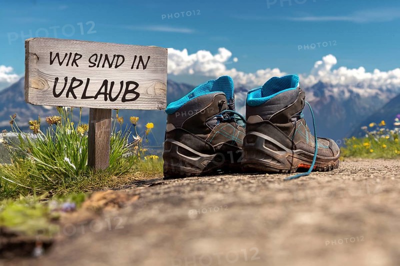 Symbolic image of company holidays/summer holidays: Hiking boots in front of an alpine backdrop and a sign saying WE ARE ON HOLIDAY