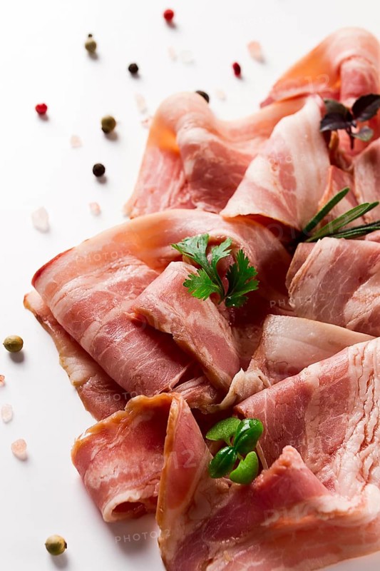Raw bacon, sliced, with micro greenery and spices, on a white background, close-up