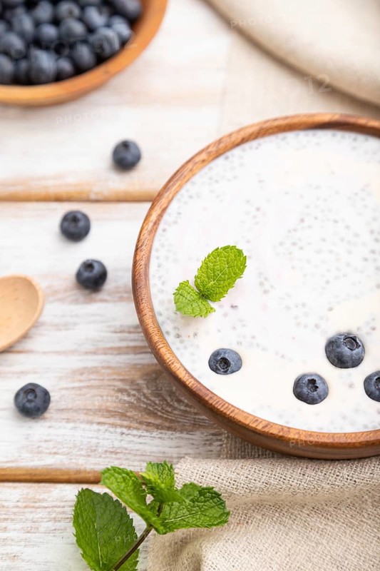 Yogurt with blueberry in wooden bowl on white wooden background and linen textile. Side view, close up, selective focus