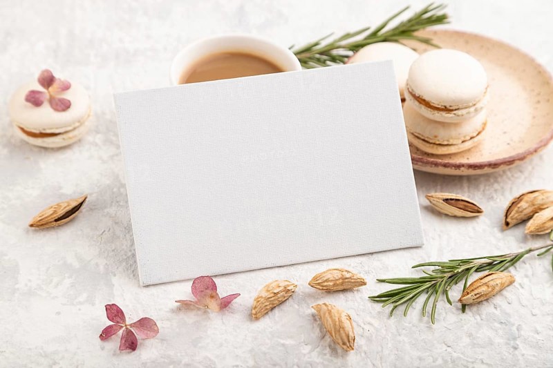 White business card mockup with cup of coffee, almonds and macaroons on gray concrete background. Blank, side view, still life