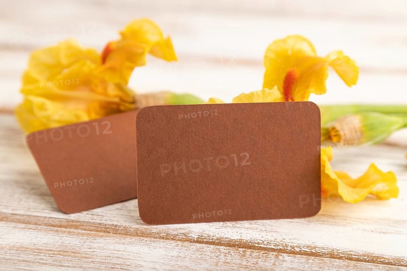 Brown business card with iris yellow flowers on white wooden background. side view, copy space, mockup, template, spring, summer minimalism concept