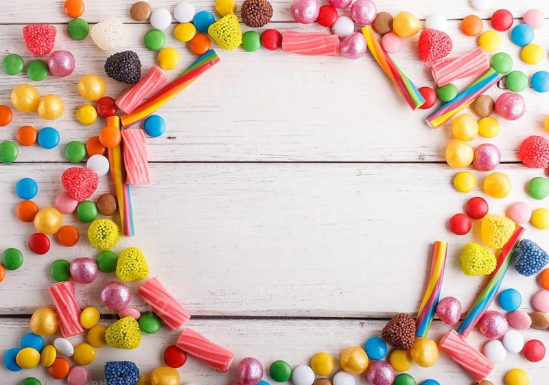 Colorful frame of multicolored candies on white wooden background. Circle copy space, top view, flat lay