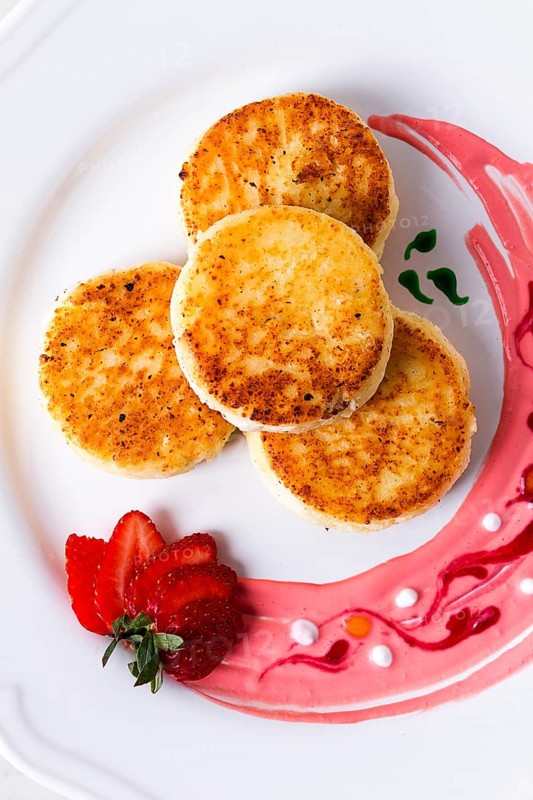 Cottage cheese pancakes, on a white plate decorated with sauce, fresh strawberry berry, close-up, no people
