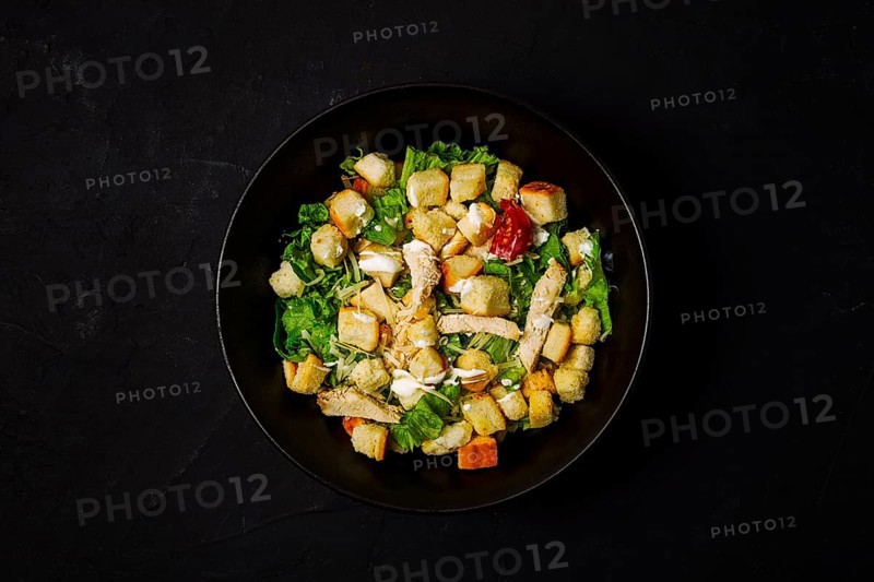 Fresh traditional Caesar salad, with chicken, on a black background, Top view, dark background, horizontal no people