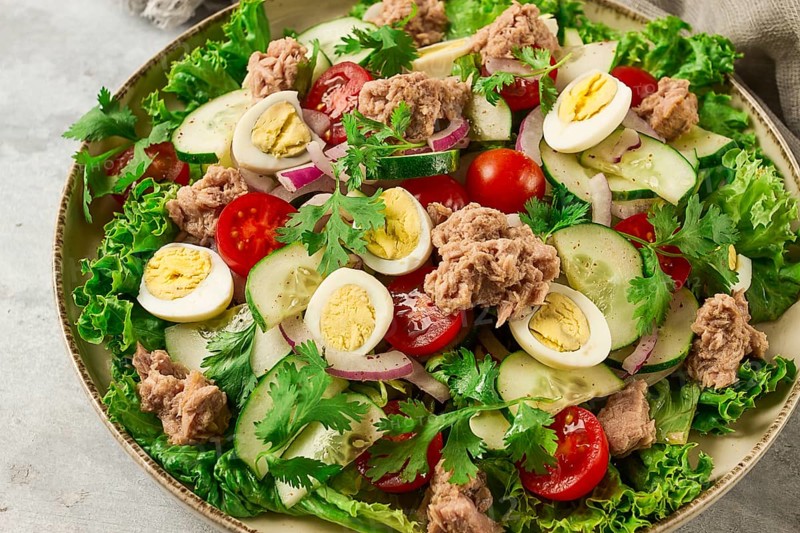 Tuna salad, vegetable salad with quail eggs, lettuce, red onion and cucumbers, on a light gray table, keto food, lifestyle, healthy eating, selective focus, top view, no people