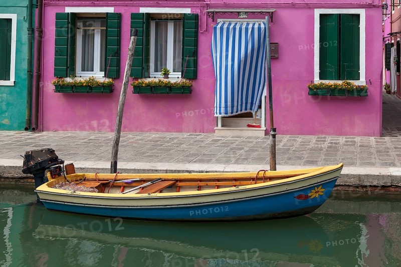Colourful boat in front of a pink house with a striped cover and green shutters on the canal, Burano Island, Italy, Europe