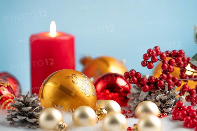 Christmas decorations with red and gold baubles, a burning candle and pine cones against a blue background