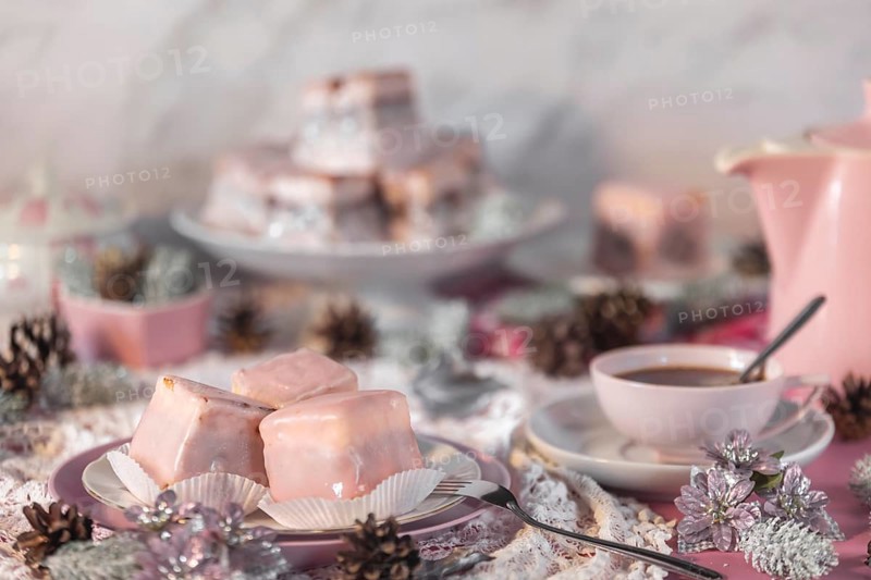 Pink glazed cakes, punch doughnuts surrounded by winter decorations, coffee pot and cup of coffee