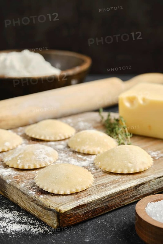 Fresh pasta is being prepared on a wooden board with flour and butter visible, alongside a rolling pin and herbs. The process highlights the art of traditional cooking and crafting.