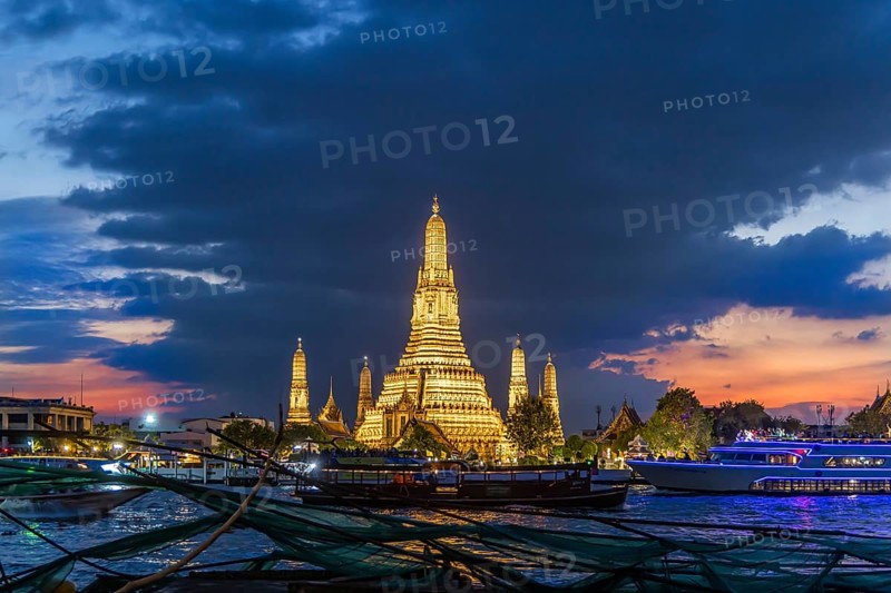 Wat Arun, Temple of Dawn at sunset with dark clouds. Boats on the Chao Phraya river. Tourist attraction in Bangkok, Thailand, Asia