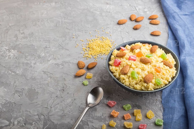 Millet porridge with candied fruits and almonds in blue ceramic bowl on a gray concrete background and blue linen textile. Side view, copy space