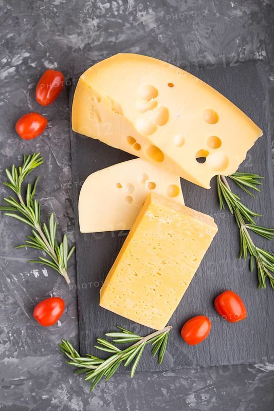 Various types of cheese with rosemary and tomatoes on black slate board on a black concrete background. Top view, flat lay, close up