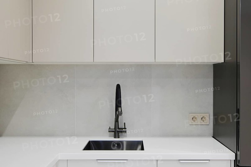 A contemporary kitchen showcases clean lines with minimalistic cabinetry in light colors. The stainless steel sink is the focal point against a smooth wall
