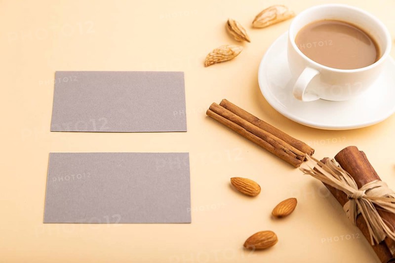 Composition of gray paper business cards, almonds, cinnamon and cup of coffee. mockup on orange background. Blank, side view, still life, copy space
