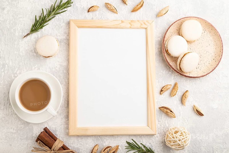 White wooden frame mockup with cup of coffee, almonds and macaroons on gray concrete background. Blank, top view, flat lay, still life