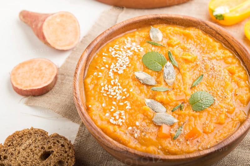 Sweet potato or batata cream soup with sesame seeds in a wooden bowl on a white wooden background with linen textile. side view, close up, selective focus