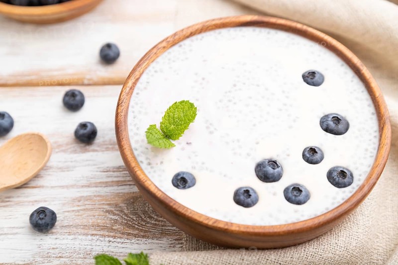 Yogurt with blueberry in wooden bowl on white wooden background and linen textile. Side view, close up, selective focus