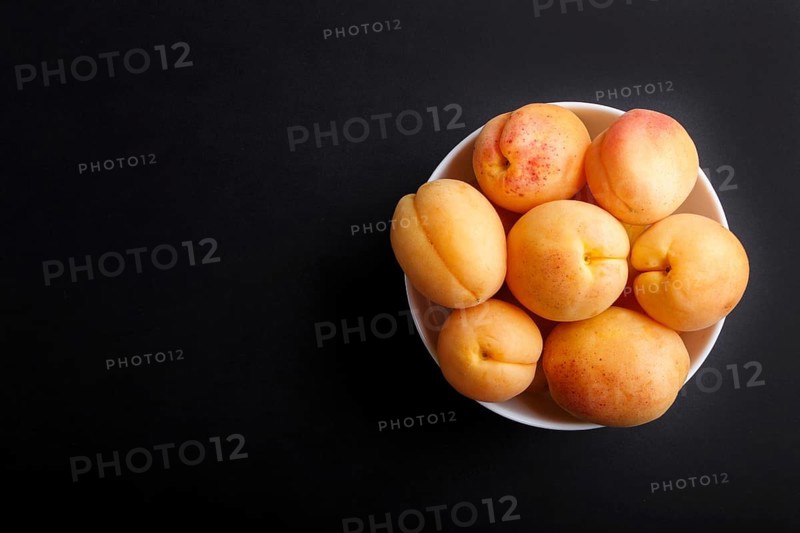 Fresh orange apricots in white bowl on black background. top view, flat lay, copy space