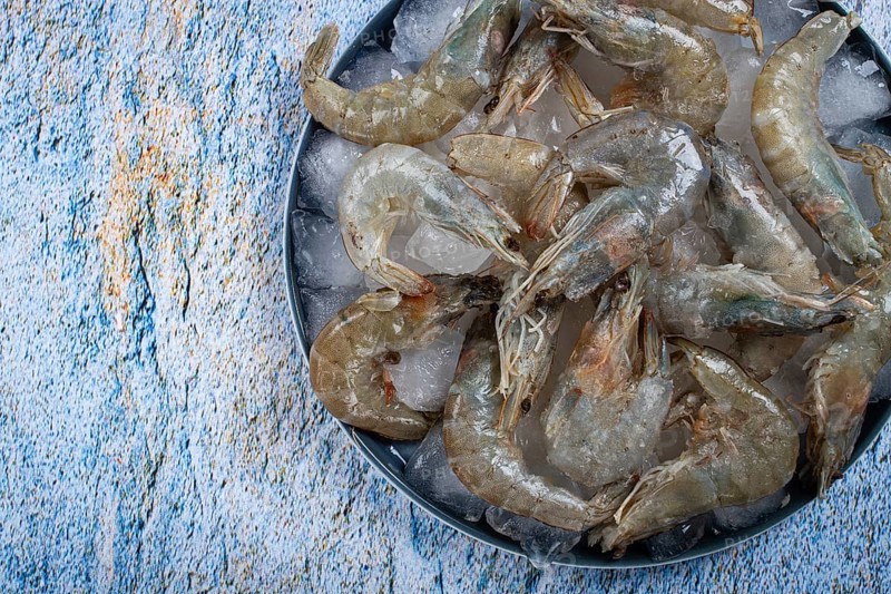 Fresh raw shrimp, spread on ice with lemon and cilantro slices on a marble surface, ready to cook, no people