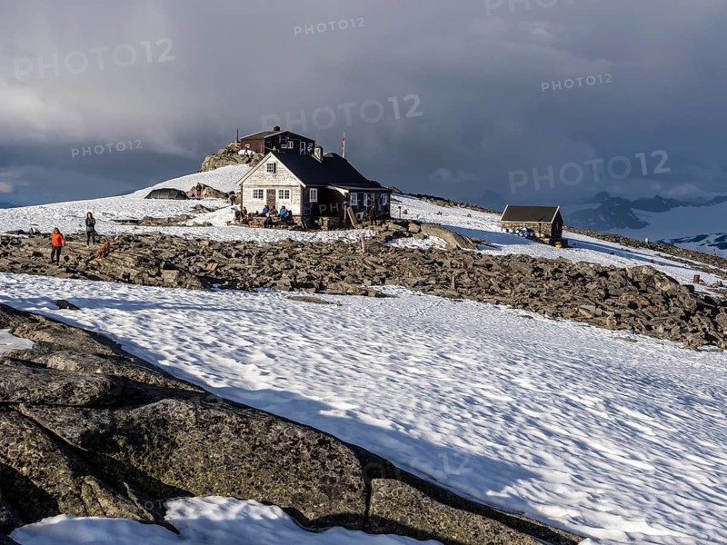 Mountain hut on top of mountain Fannaråken, hikers sit outside the hut, enjoy the sun, Jotunheimen National Park, Norway, Europe