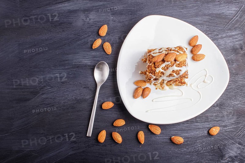 Pie with caramel, white milk sauce and almonds on a white plate on a black wooden background. top view, copy space