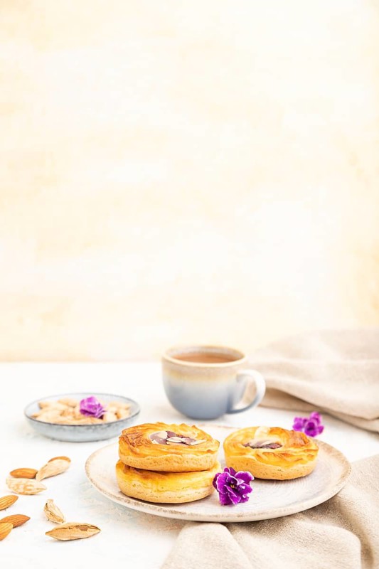 Small cheesecakes with jam and almonds with cup of coffee on a white concrete background and linen textile. Side view, copy space