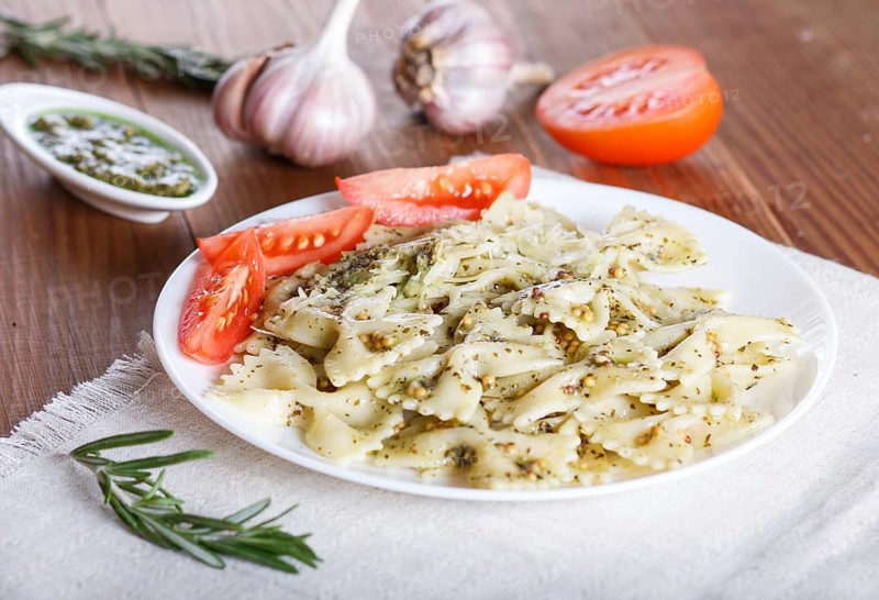 Farfalle pasta with pesto sauce, tomatoes and cheese on a linen tablecloth on a brown wooden background. close up, selective focus