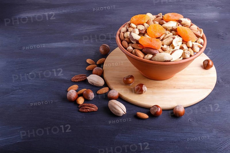 Mixed different kinds of nuts in ceramic bowl on black wooden background with copy space. hazelnut, brazil nut, almond, pumpkin seeds, cashew