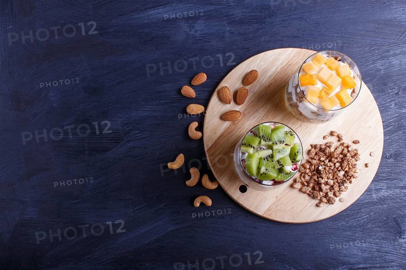 Dessert with greek yogurt, granola, almond, cashew, kiwi and persimmon on black wooden background. top view, copy space